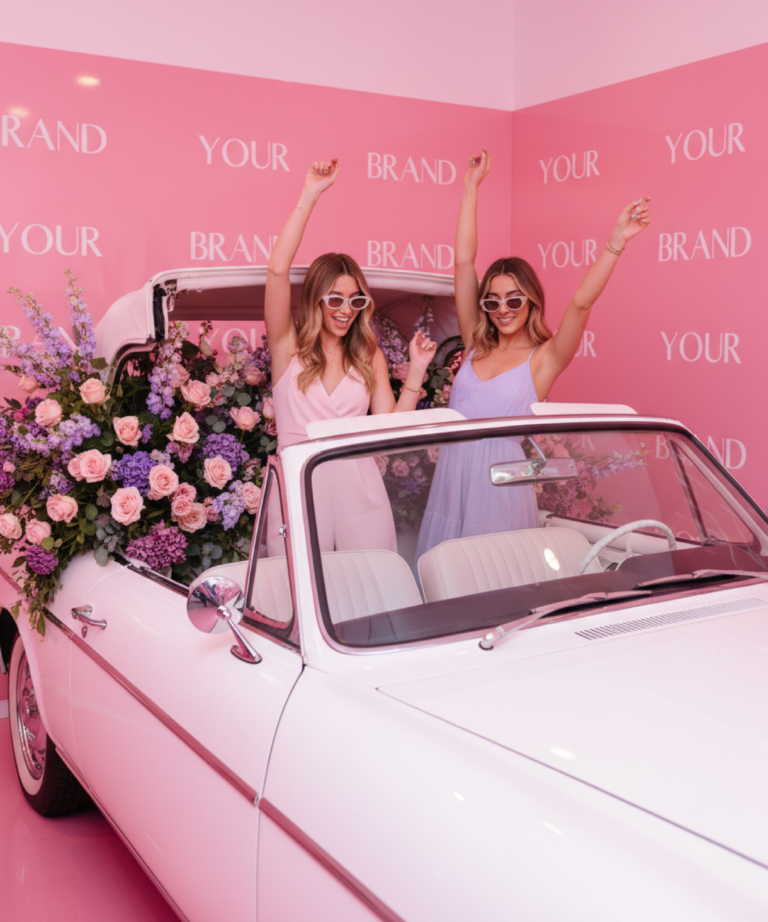 Décor événementiel sur mesure avec voiture vintage fleurie servant de photocall lors d’une activation de marque, dans un univers rose immersif et photogénique.