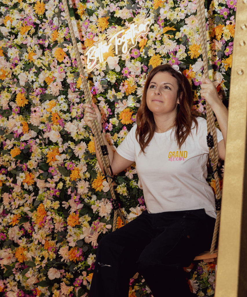 Décor événementiel immersif avec balançoire dorée et mur de fleurs, conçu par Le Grand Décor