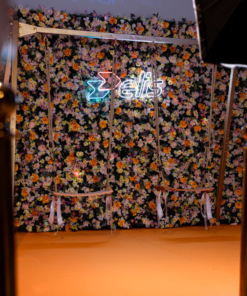 Photocall événementiel immersif avec mur de fleurs, balançoire dorée et néon personnalisé
