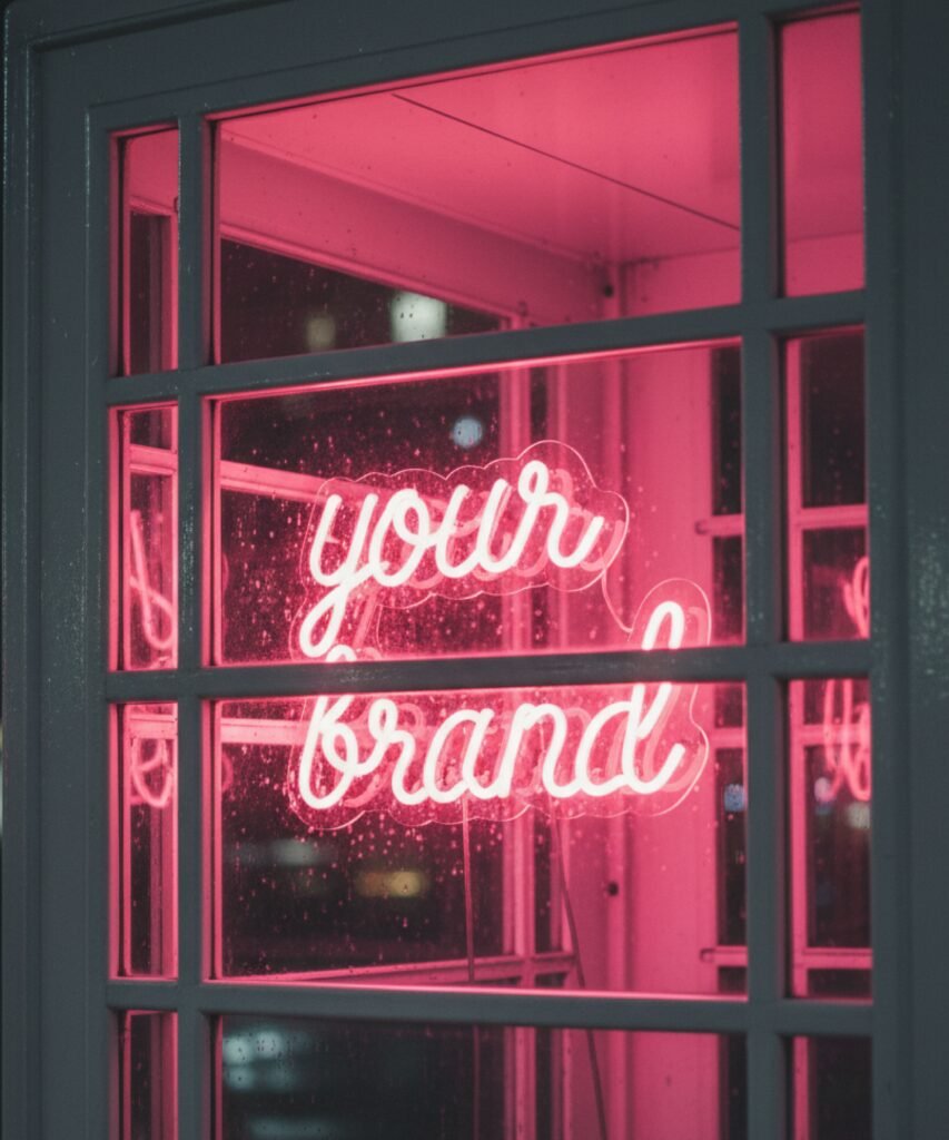 Néon rose personnalisé visible à travers la vitre d’une cabine téléphonique blanche.