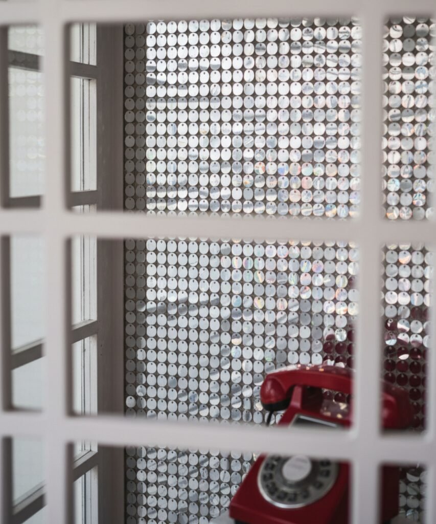 Intérieur cabine téléphonique avec mur sequins argentés et téléphone vintage rouge.